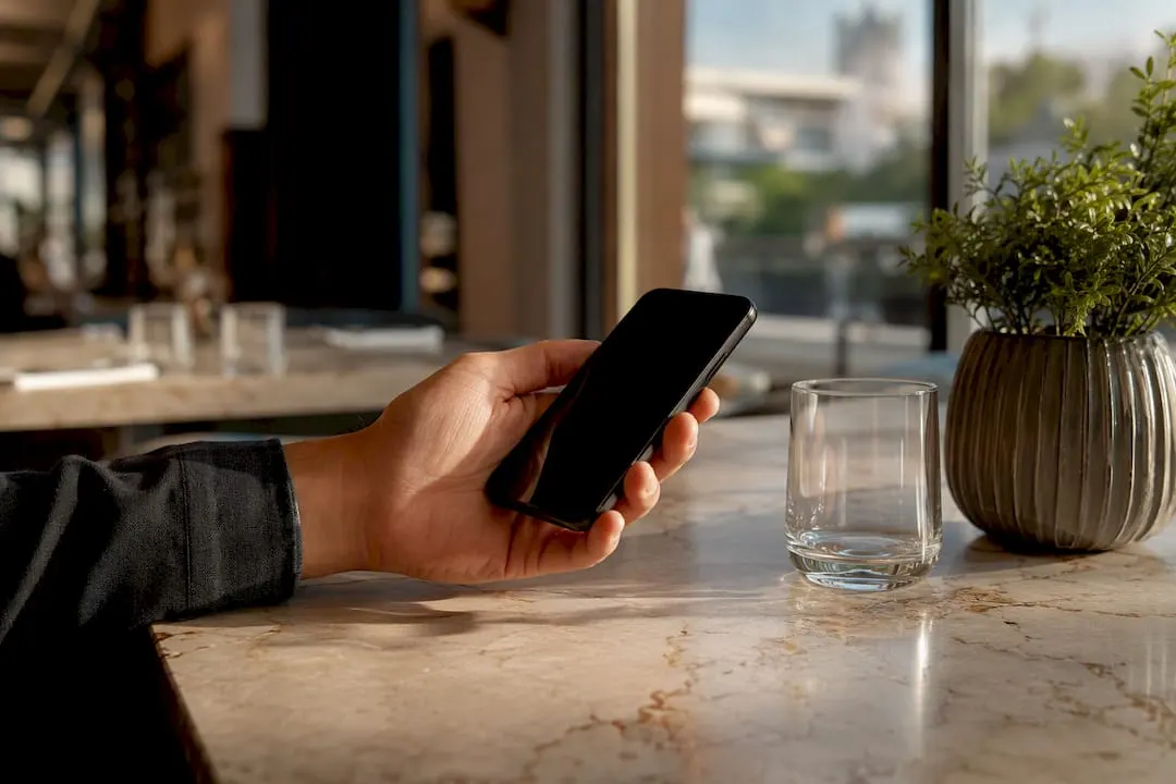Eine Hand hält ein Handy mit ausgeschaltetem Display, das auf der Theke im Café liegt.